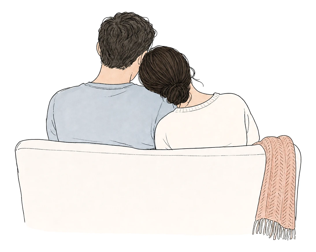 A couple sit close together on a couch, the woman resting her head on the man's shoulder.